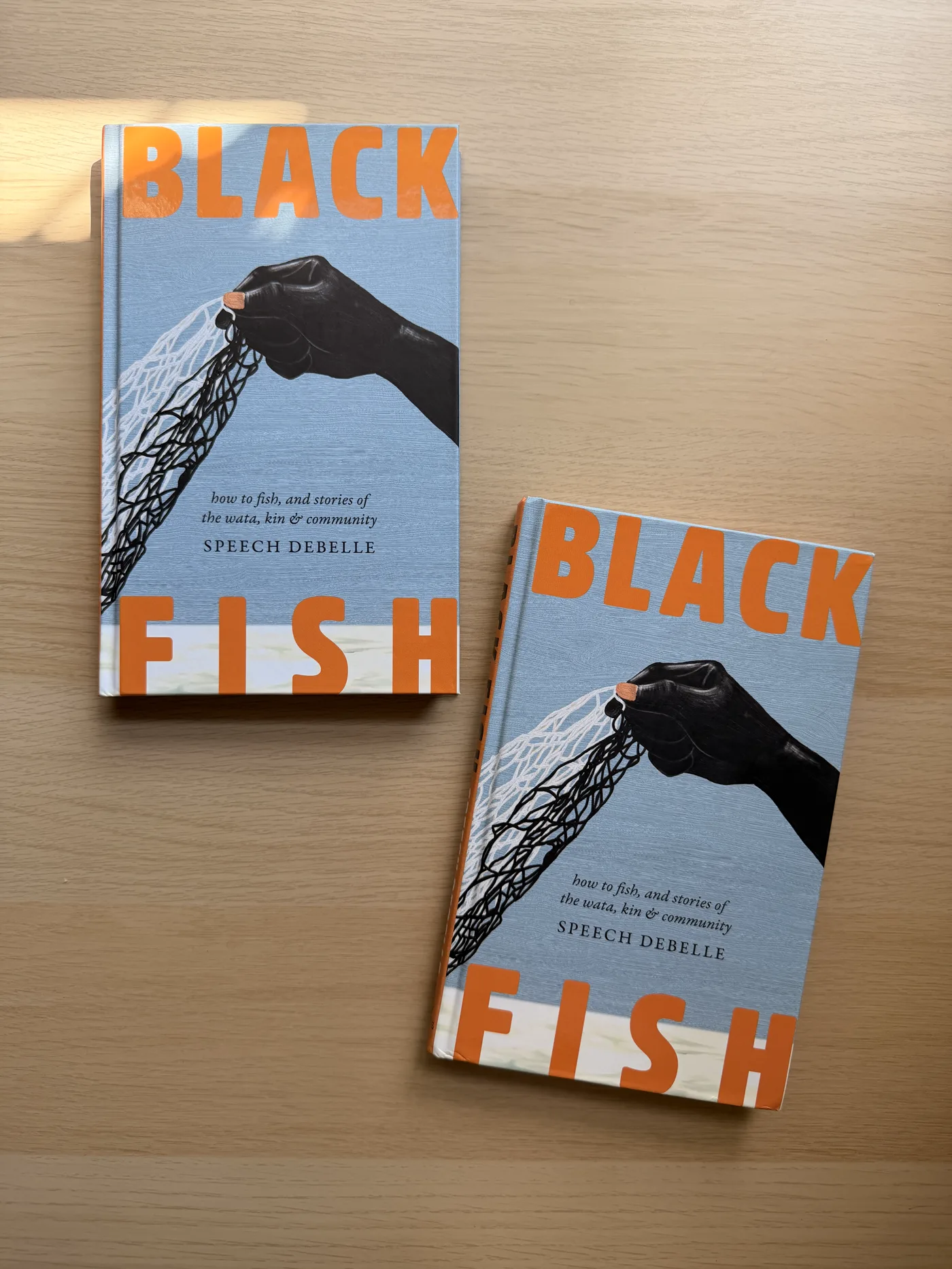 Two published Black Fish books by Speech Debelle on a wooden table.